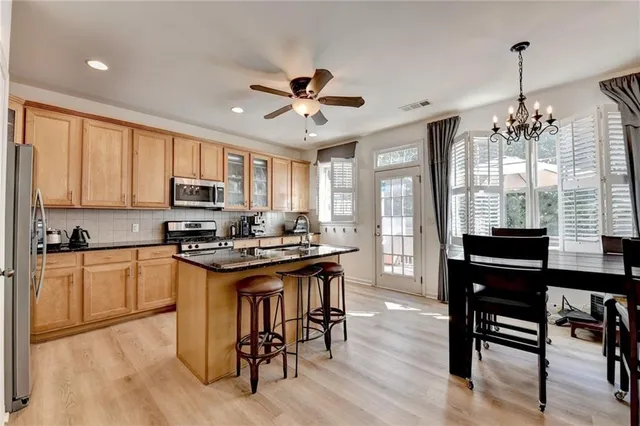 a kitchen with stainless steel appliances granite countertop a stove top oven a refrigerator a sink and white cabinets with wooden floor