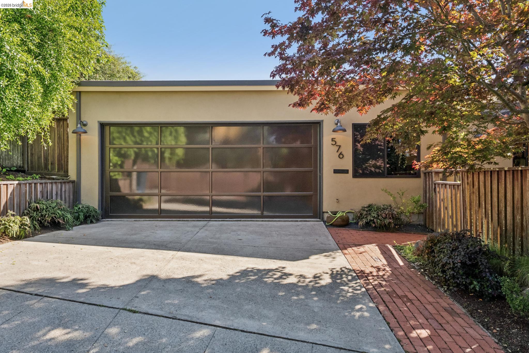 576 Vistamont Avenue Berkeley, CA 94708 - Photo 32 of 33 Modern stucco exterior featuring a glass panel garage door, concrete driveway, brick walkway, and mature landscaping