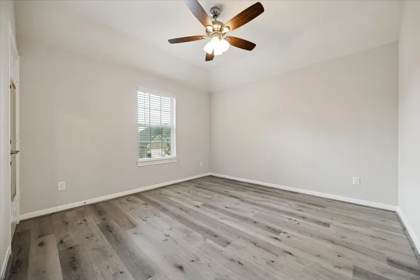 an empty room with wooden floor ceiling fan and window