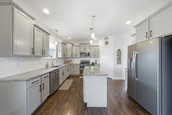 a kitchen with stainless steel appliances a refrigerator a sink dishwasher a stove and white cabinets with wooden floor