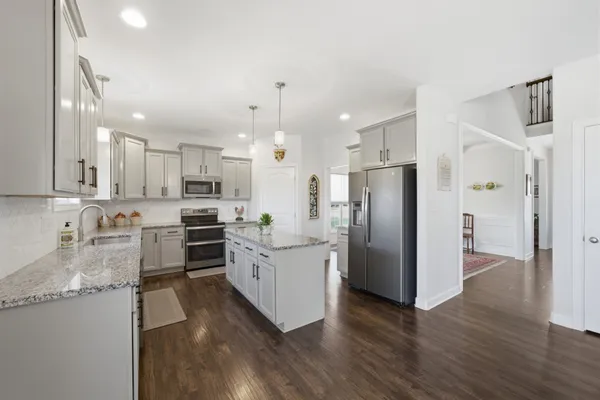 a kitchen with stainless steel appliances kitchen island granite countertop a refrigerator a stove a sink and white cabinets with wooden floor
