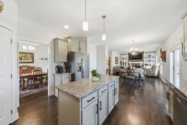 a kitchen with granite countertop a refrigerator stove oven dining table and chairs with wooden floor