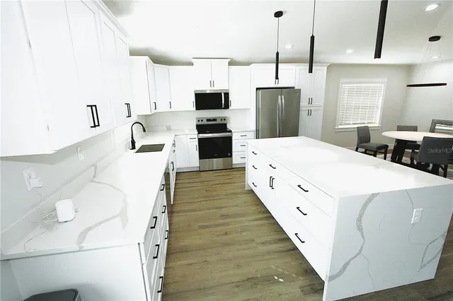 a large kitchen with kitchen island a refrigerator a stove a sink dishwasher a oven with white cabinets and wooden floor