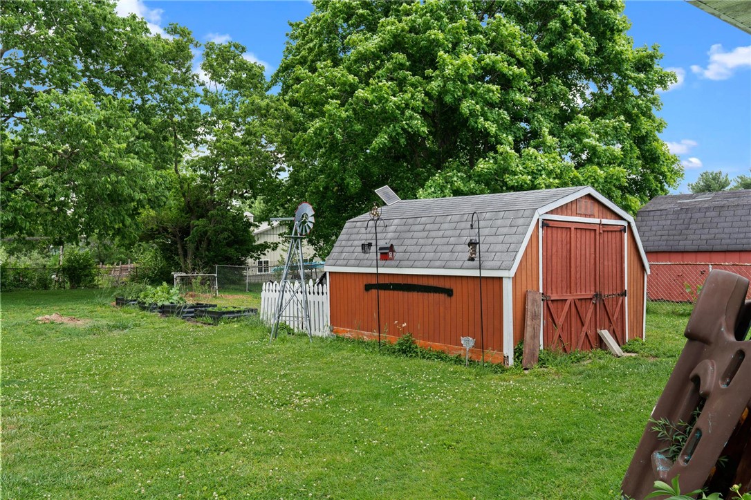 A quaint red barn with a grey roof and an old-fashioned windmill anchors this verdant backyard space.