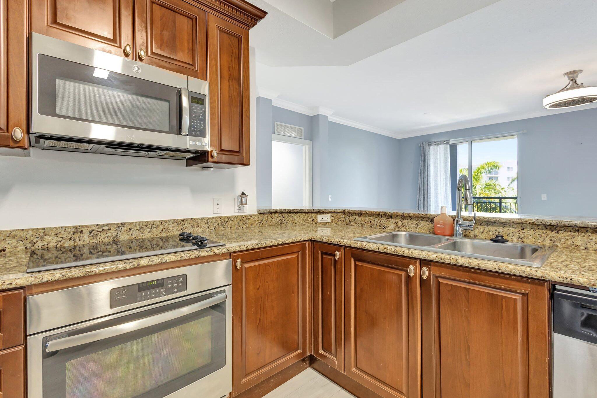 1690 Renaissance Commons Boulevard, Unit 1401 Boynton Beach, FL 33426 - Photo 5 of 41 a kitchen with stainless steel appliances granite countertop a sink and a microwave