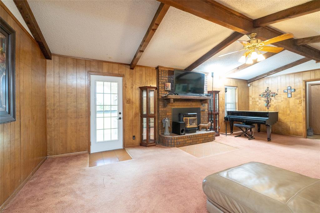 151 County Road 3699 Springtown, TX 76082 - Photo 5 of 35 Living space featuring wood paneling, a brick fireplace, exposed ceiling beams, a ceiling fan with integrated lighting, and a glass-paneled exterior door