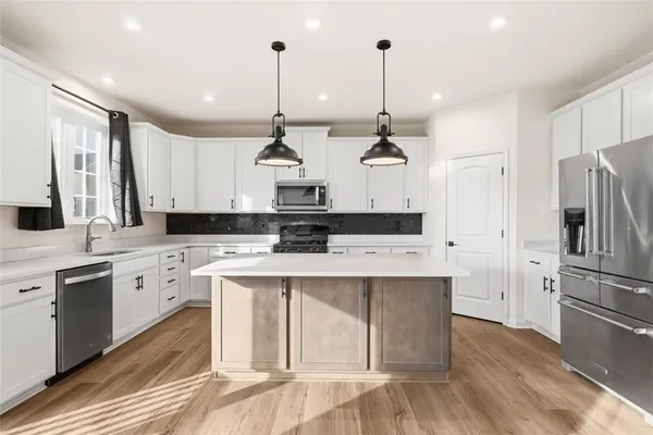 a kitchen with stainless steel appliances kitchen island a refrigerator a sink dishwasher a stove and white cabinets with wooden floor