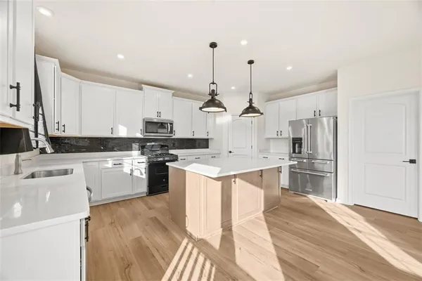 a kitchen with stainless steel appliances kitchen island granite countertop a sink a stove a refrigerator and white cabinets