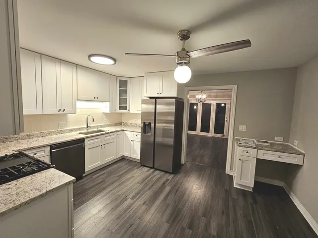 a kitchen with stainless steel appliances granite countertop a refrigerator a sink dishwasher a stove and white countertops with wooden floor