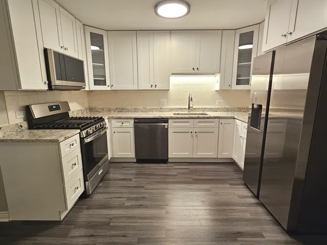 a kitchen with stainless steel appliances granite countertop a stove top oven a refrigerator a sink and dishwasher with wooden floor