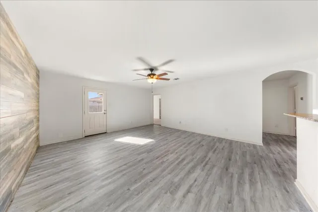 an empty room with wooden floor chandelier fan and windows