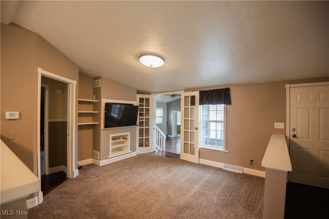 4594 Center Road Andover, OH 44003 - Photo 11 of 39 Unfurnished living room featuring a textured ceiling, vaulted ceiling, dark carpet, and built in shelves