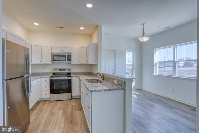 a kitchen with stainless steel appliances granite countertop a refrigerator a stove top oven a sink and dishwasher with wooden floor