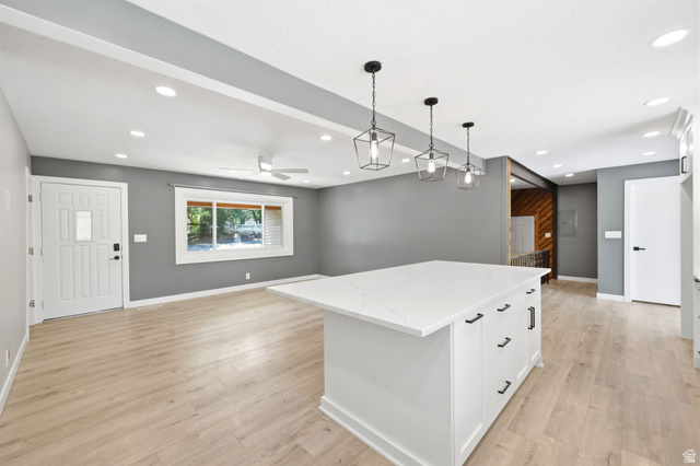 Central kitchen island with a light-toned countertop, recessed ceiling lights, wood-finish flooring, ceiling fan, and modern pendant lighting fixtures