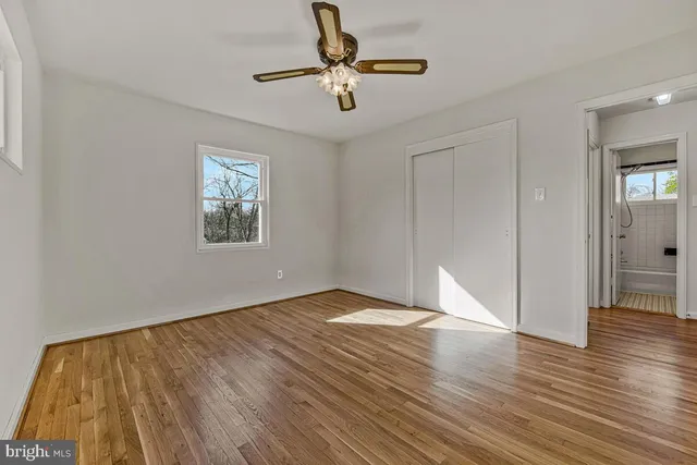 a view of an empty room with wooden floor and a ceiling fan