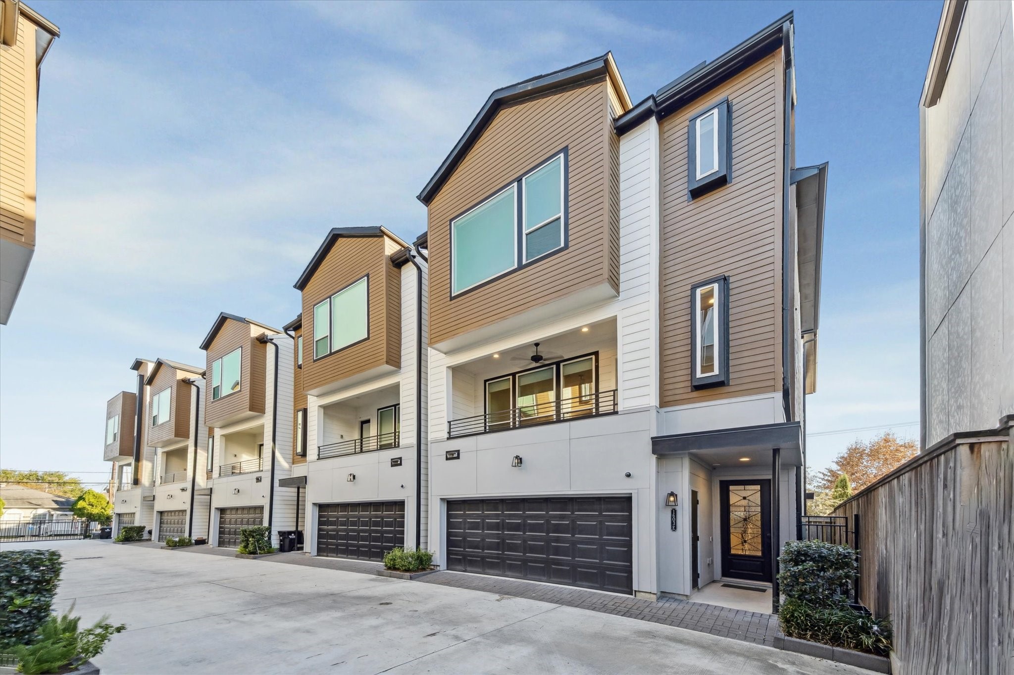 1603 Patterson Street, Unit E Houston, TX 77007 - Photo 1 of 32 Modern townhomes with a sleek design feature large windows, two-car garages, and a clean, shared driveway. The exterior is a mix of wood and white paneling, offering a contemporary and inviting look.