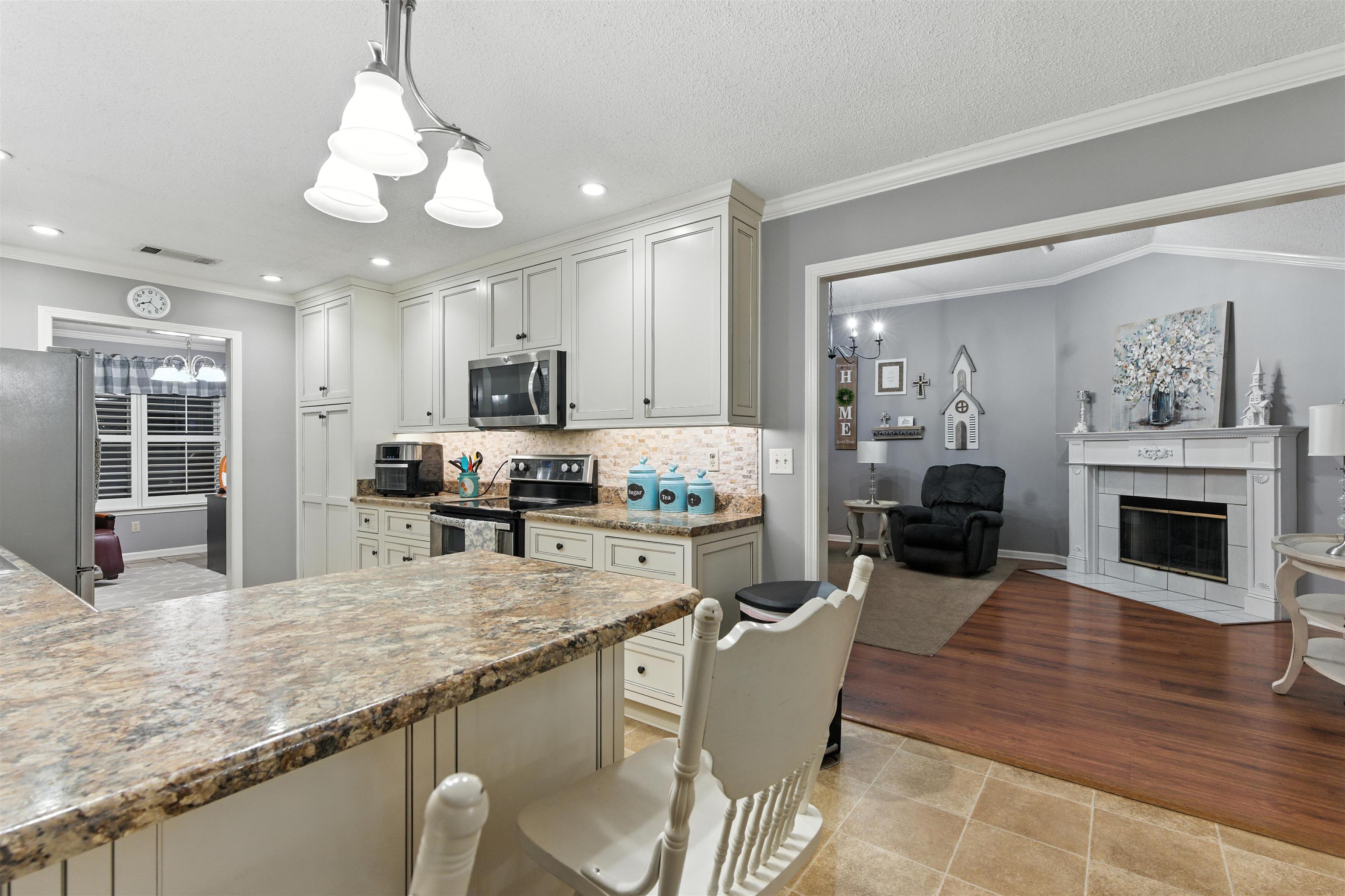 8665 Brunswick Road Millington, TN 38053 - Photo 39 of 39 Kitchen featuring a chandelier, ornamental molding, appliances with stainless steel finishes, open floor plan, and a fireplace