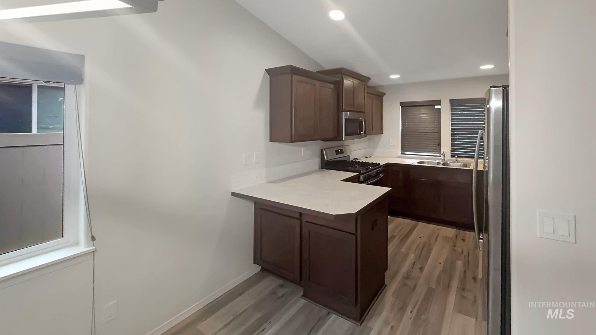 5223 Junegrass Way Caldwell, ID 83607 - Photo 2 of 16 Kitchen with dark wood finish cabinetry, light countertops, stainless steel appliances, a peninsula, and light wood-style floors