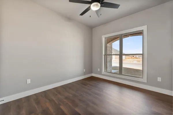 an empty room with wooden floor fan and windows