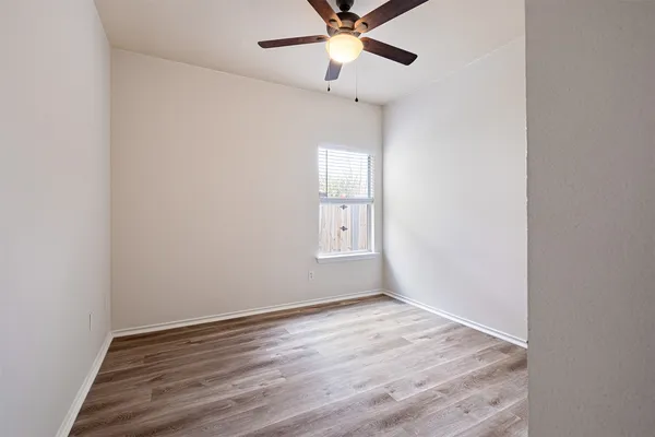 an empty room with wooden floor fan and windows