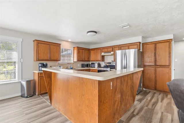 a large kitchen with stainless steel appliances granite countertop a refrigerator a sink dishwasher a stove and white countertops with wooden floor