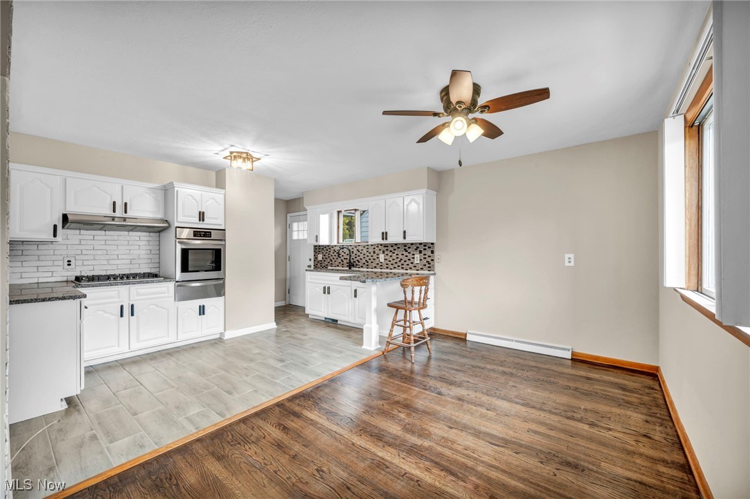 10927 Granger Road Cleveland, OH 44125 - Photo 14 of 33 Kitchen with light wood-type flooring, decorative backsplash, white cabinetry, appliances with stainless steel finishes, and dark stone countertops