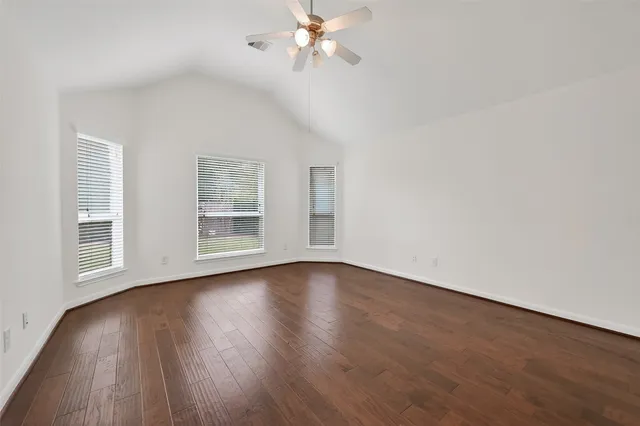 an empty room with wooden floor chandelier fan and windows