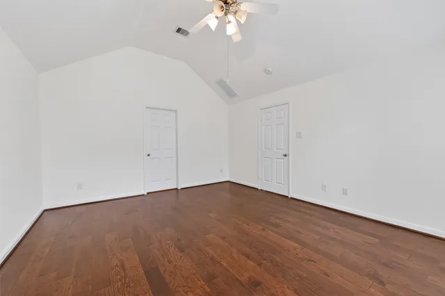 an empty room with a chandelier fan and wooden floor