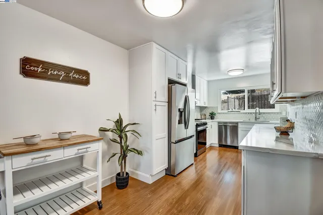 a kitchen with stainless steel appliances a refrigerator a stove a sink dishwasher and a dining table with wooden floor