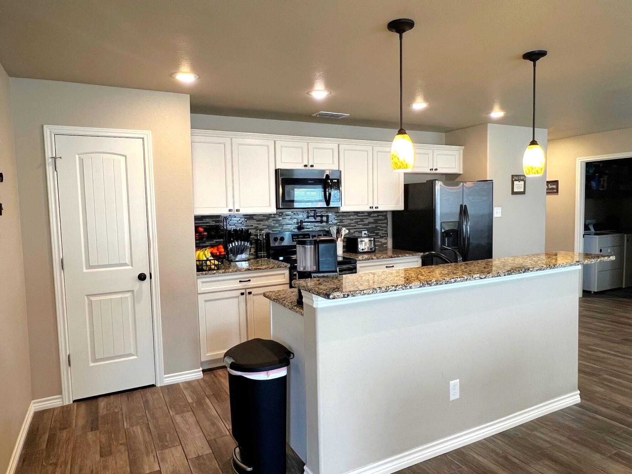 8803 10th Place Lubbock, TX 79416 - Photo 4 of 27 a kitchen with kitchen island a refrigerator a stove a microwave oven a sink with island and chairs
