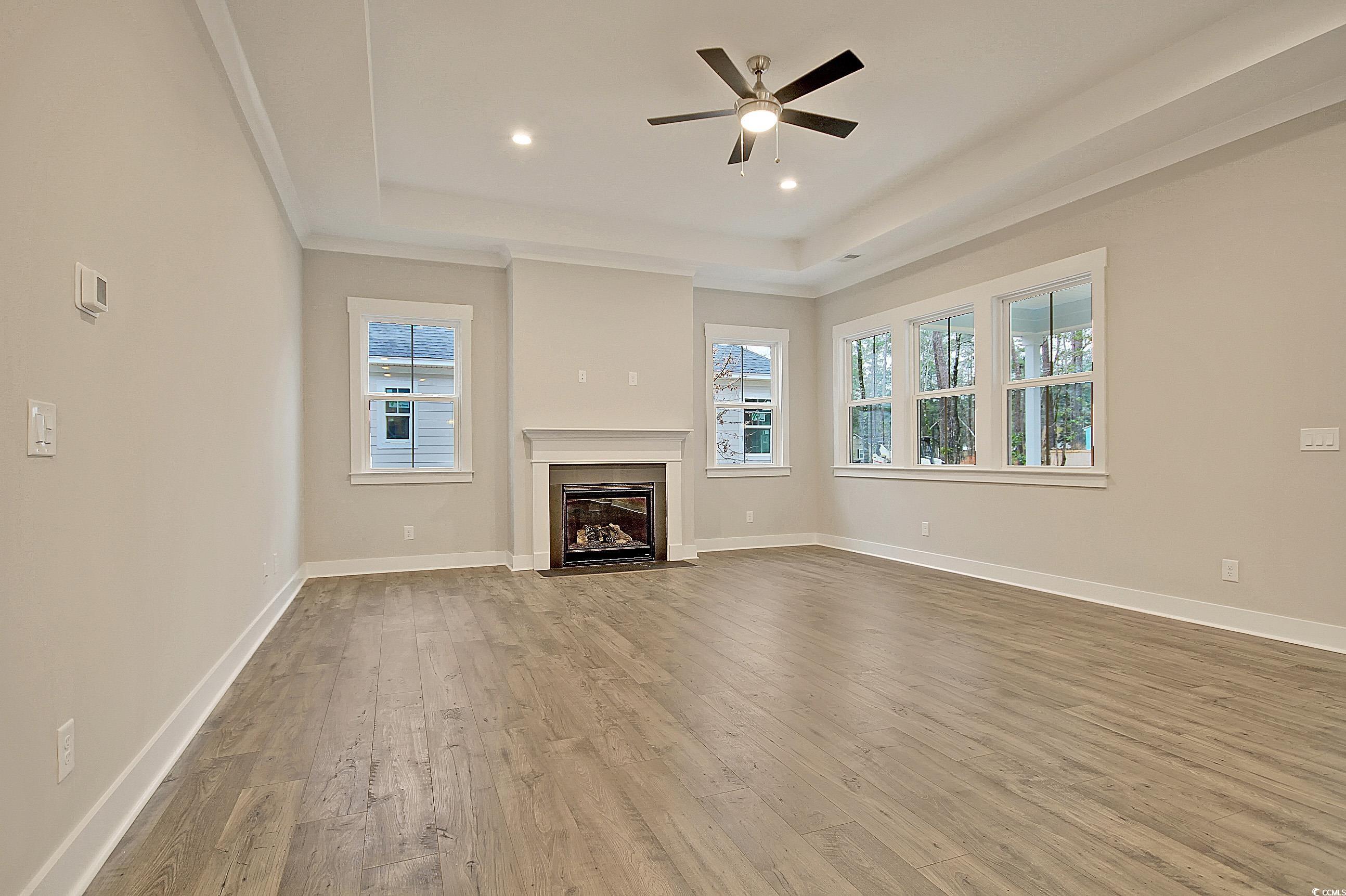 171 Pinebury Drive Georgetown, SC 29440 - Photo 5 of 30 Unfurnished living room featuring a tray ceiling, light wood finished floors, a fireplace with flush hearth, a ceiling fan, and recessed lighting