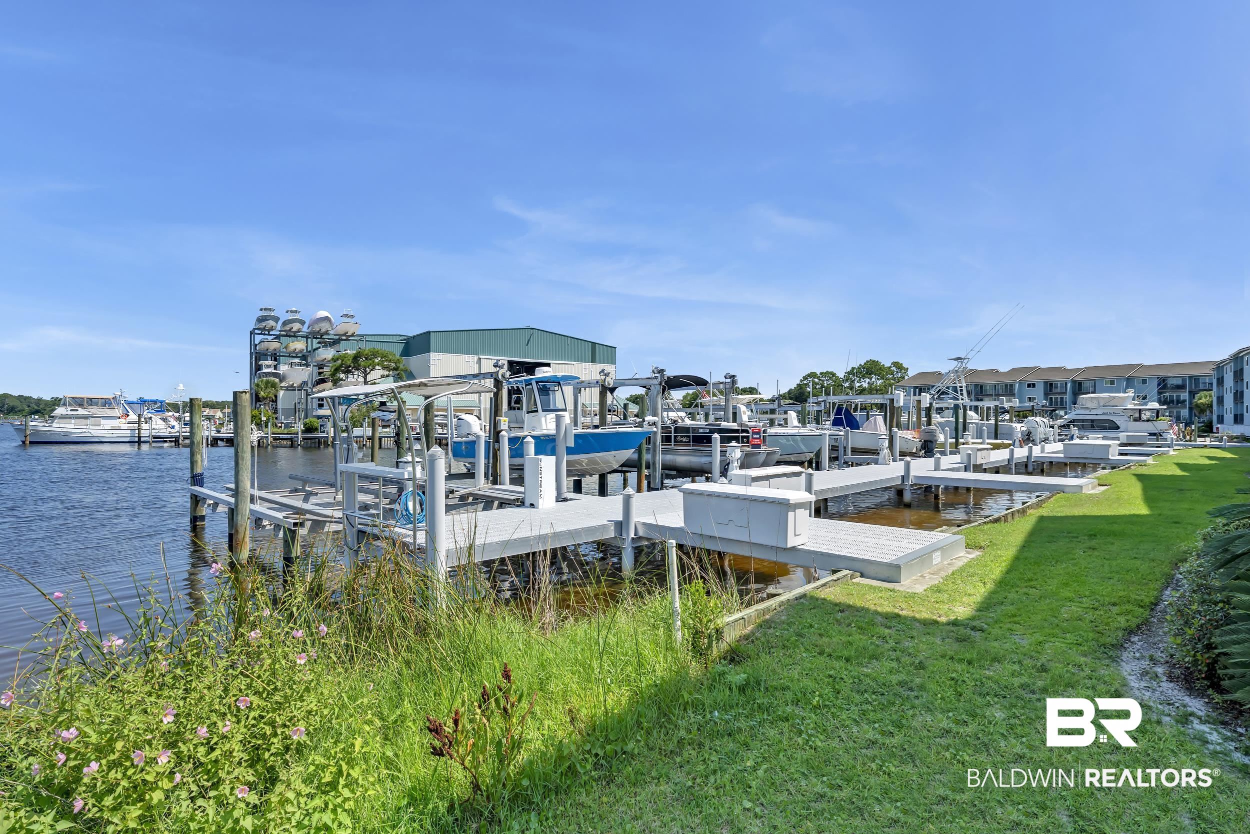 14100 River Road, Unit 211 Pensacola, FL 32507 - Photo 46 of 56 Waterfront property featuring multiple boat slips with lifts, a manicured green lawn, and a clear blue sky
