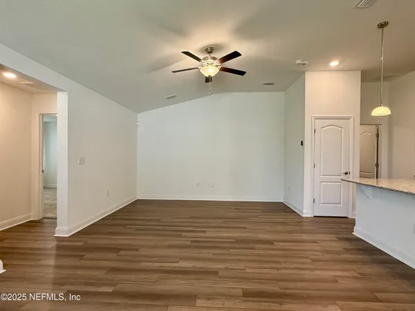 a view of an empty room with wooden floor and a ceiling fan