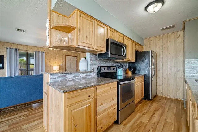 a kitchen with stainless steel appliances granite countertop a refrigerator a stove top oven a sink and dishwasher with wooden floor