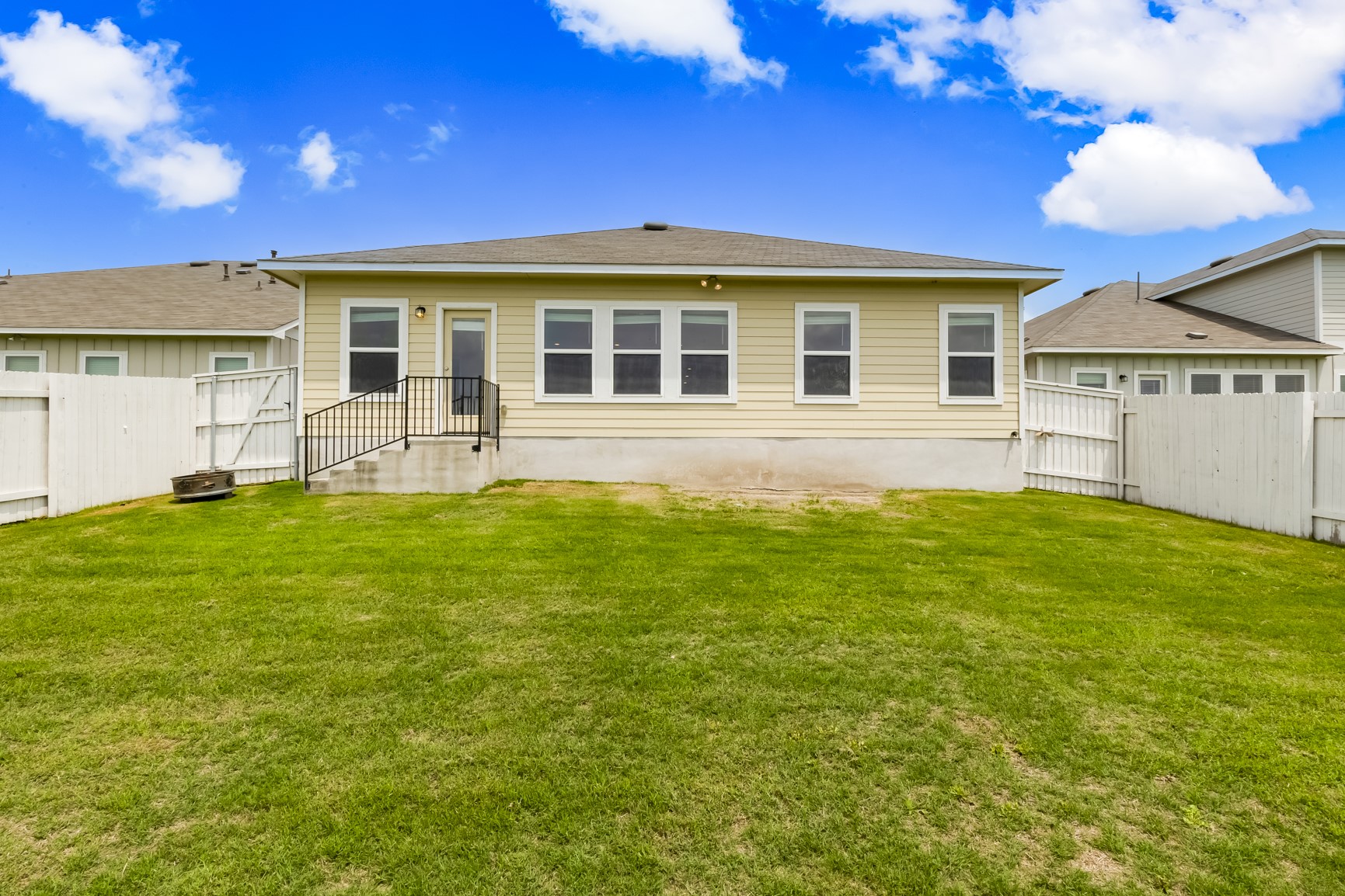 2721 Winding Creek Road Kyle, TX 78640 - Photo 26 of 27 Expansive lawn area featuring a light-colored siding exterior, multiple windows, a rear entry door, and a concrete patio with black metal railings