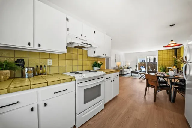 a kitchen with a stove a sink and white cabinets with wooden floor