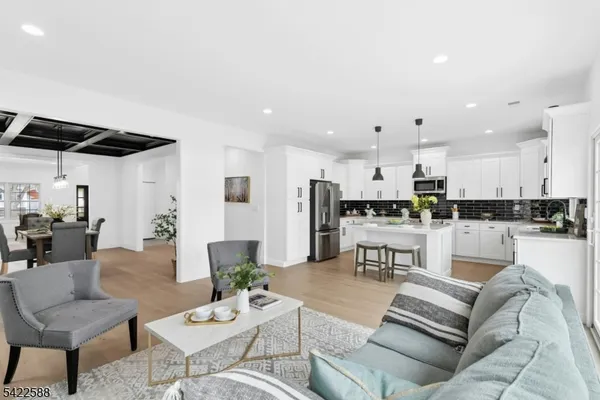 a living room with white couches and kitchen view with wooden floor