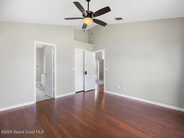 an empty room with wooden floor fan and windows