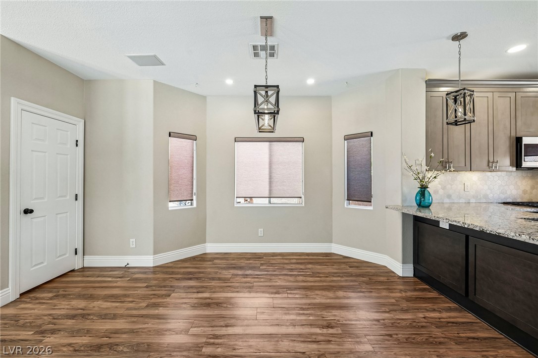 1176 Butternut Ranch Court Henderson, NV 89052 - Photo 9 of 60 Rich hardwood-style flooring extends across an open-concept dining space, anchored by unique modern lighting fixtures.