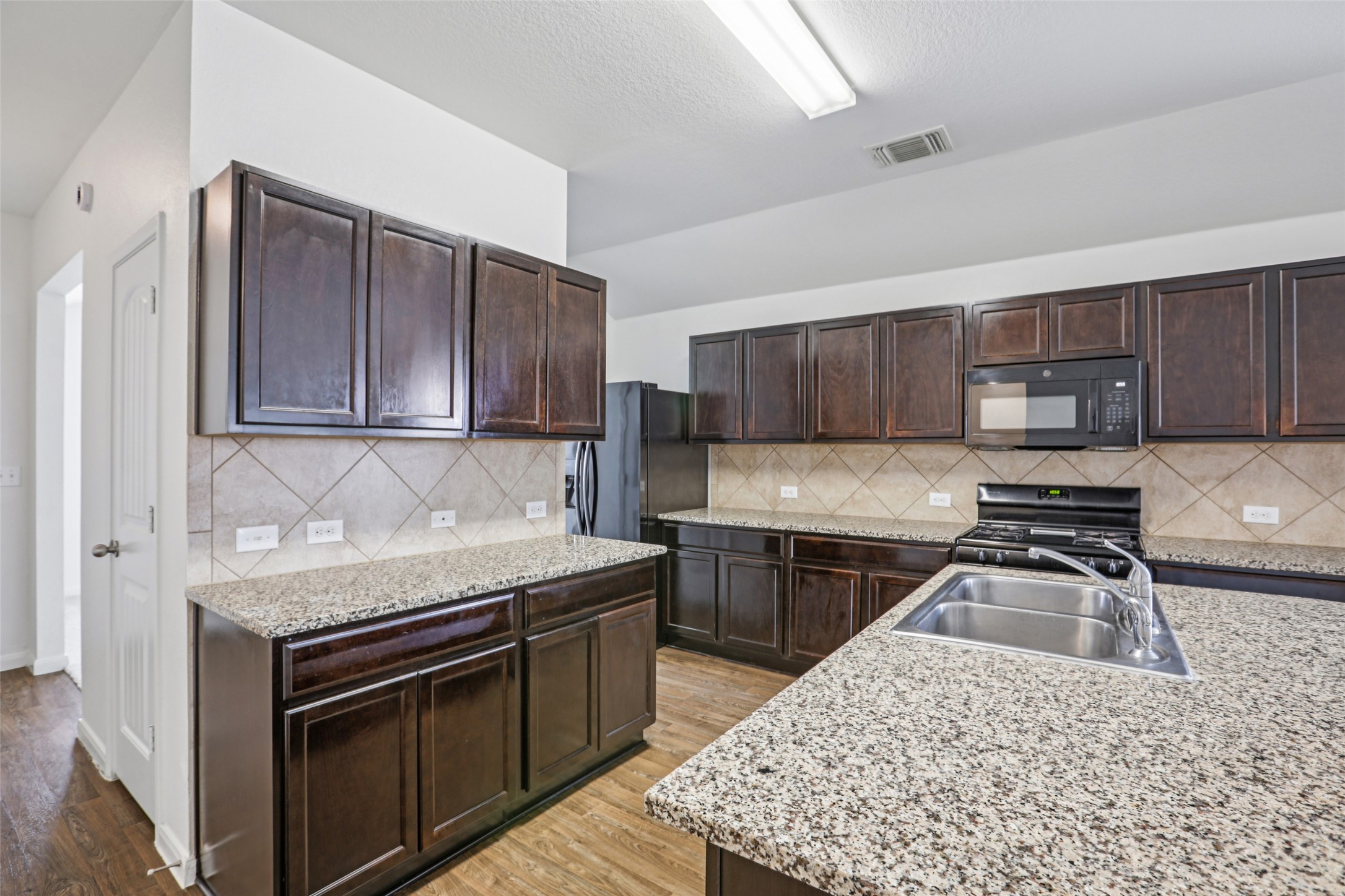 221 Alpha Kyle, TX 78640 - Photo 10 of 37 Kitchen featuring black appliances, light wood-style floors, dark wood finish cabinetry, decorative backsplash, and light stone countertops