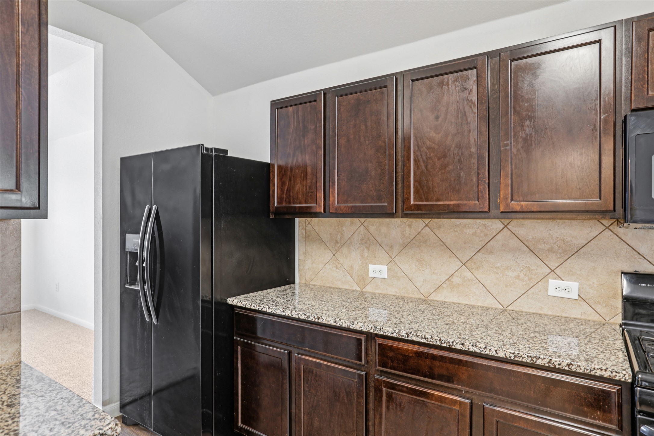 221 Alpha Kyle, TX 78640 - Photo 12 of 37 Kitchen featuring dark wood finish cabinets, light stone counters, black appliances, and vaulted ceiling