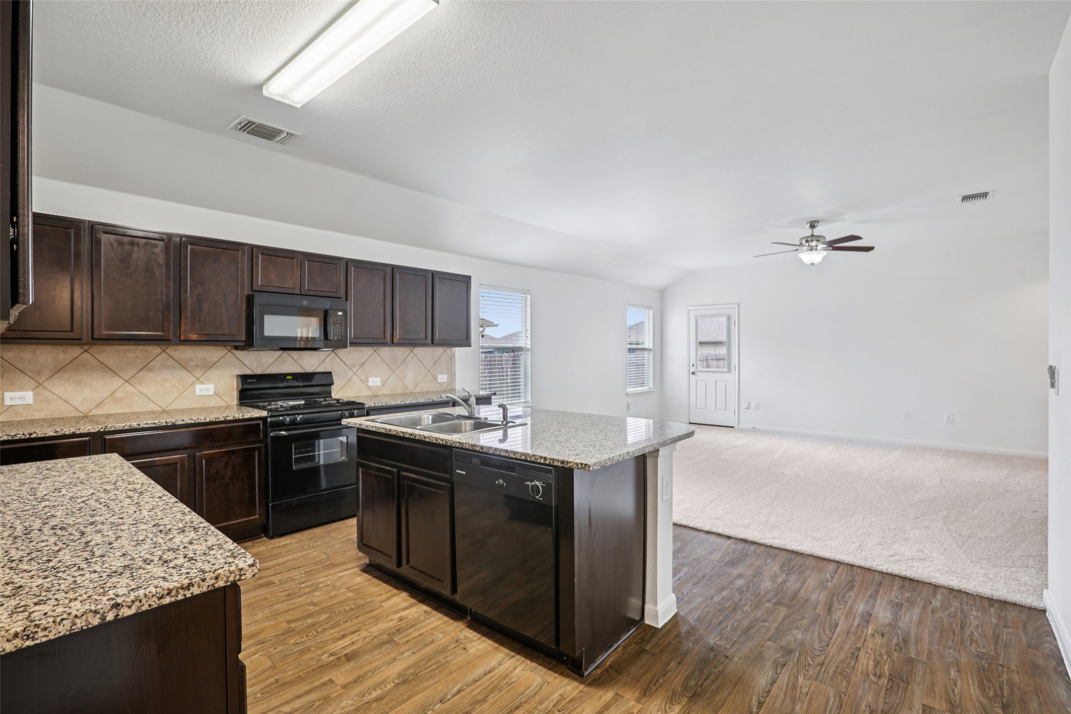 221 Alpha Kyle, TX 78640 - Photo 7 of 37 Kitchen with dark wood finish cabinetry, black appliances, light stone counters, an island with sink, and light wood-style flooring
