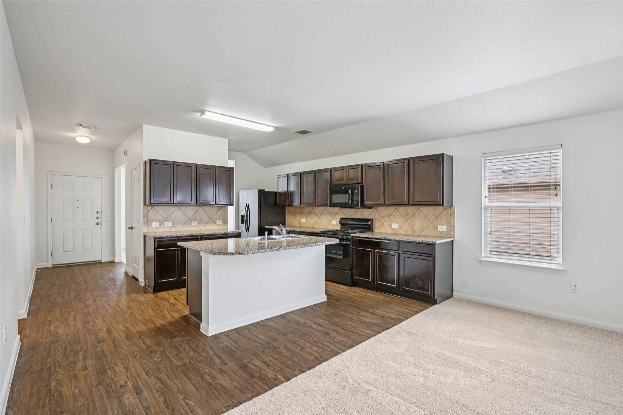 221 Alpha Kyle, TX 78640 - Photo 8 of 37 Kitchen featuring dark wood finish cabinetry, black appliances, light stone counters, lofted ceiling, and a kitchen island with sink