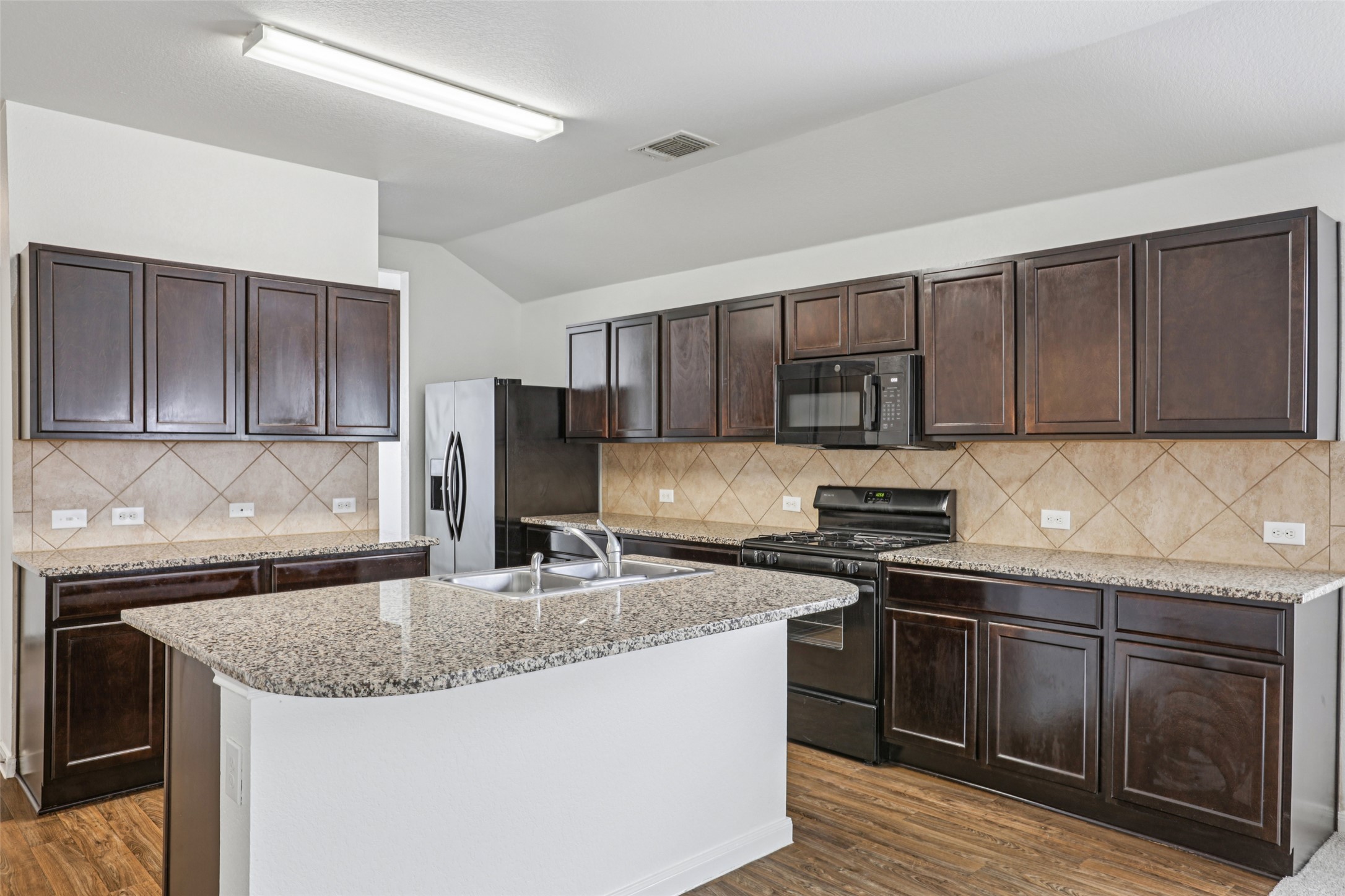 221 Alpha Kyle, TX 78640 - Photo 9 of 37 Kitchen featuring dark wood finish cabinetry, black appliances, vaulted ceiling, a center island with sink, and dark wood finished floors