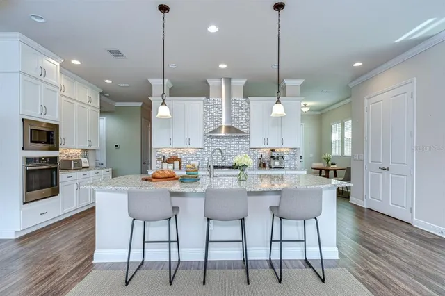 a kitchen with stainless steel appliances kitchen island granite countertop a dining table chairs sink and cabinets