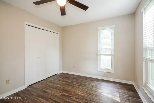 an empty room with wooden floor fan and windows