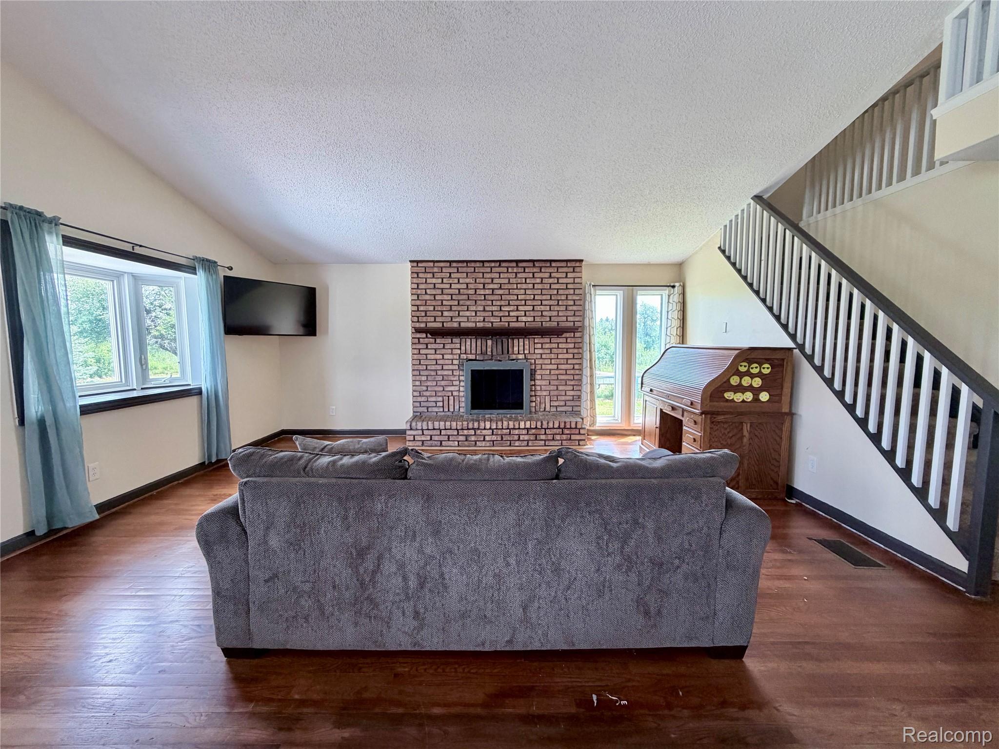 10865 Norman Road Yale, MI 48097 - Photo 9 of 23 Living area featuring a brick fireplace with a wood mantle, wood-finish flooring, and a prominent staircase with white balusters and dark handrails