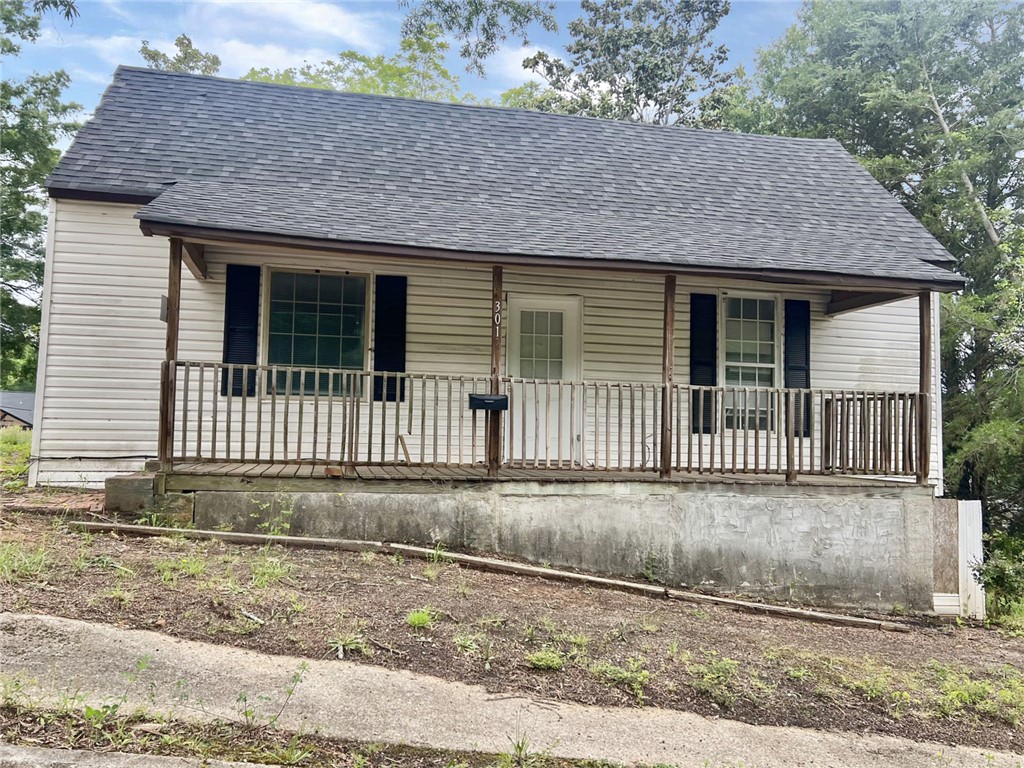 Charming home with an inviting front porch and classic white siding, nestled amongst mature trees.