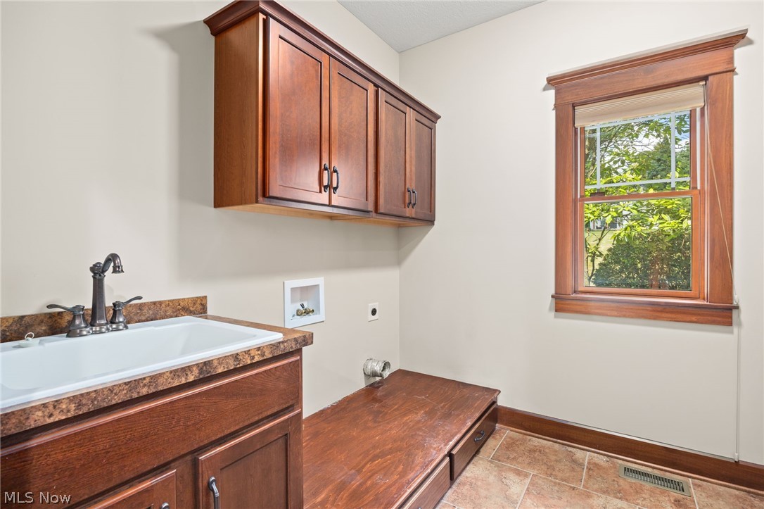 6925 River Styx Road Medina, OH 44256 - Photo 25 of 49 Utility room featuring a built-in sink with a dark bronze faucet, wood-finish cabinetry, a window with wood trim, and tile flooring