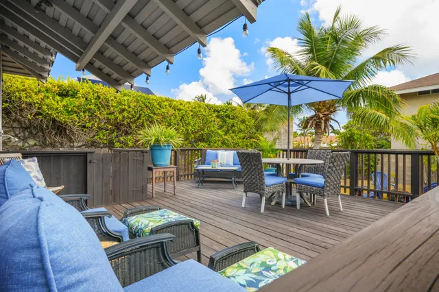 a view of a patio with couches table and chairs under an umbrella with a small yard